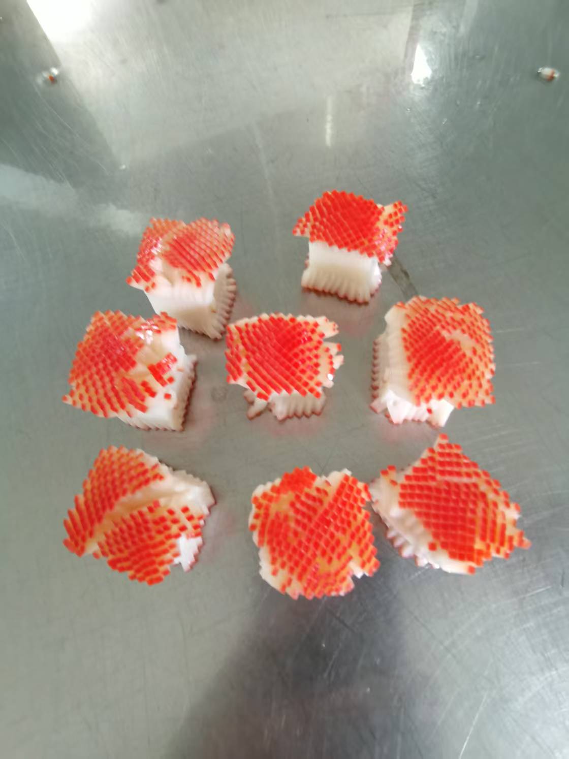Six orange and white flower-cut crab stick pieces on a metal surface